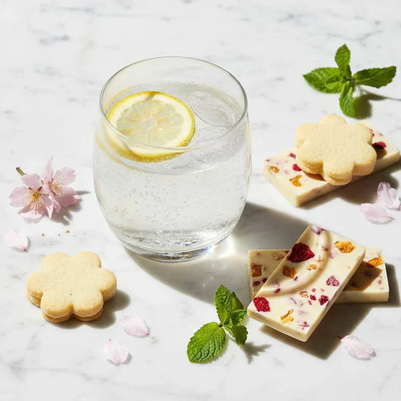 Composizione fresca di drink agrumati e snack dai toni pastello su marmo bianco, anteprima primavera 2026.