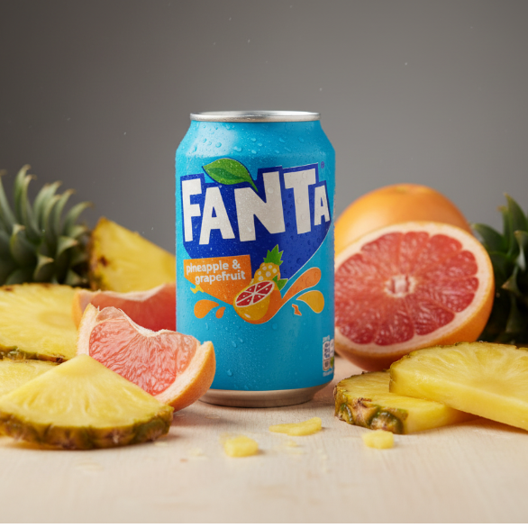 Lattina di Fanta Ananas & Pompelmo UK circondata da fette di ananas e pompelmo fresco, enfatizzando gli ingredienti naturali.